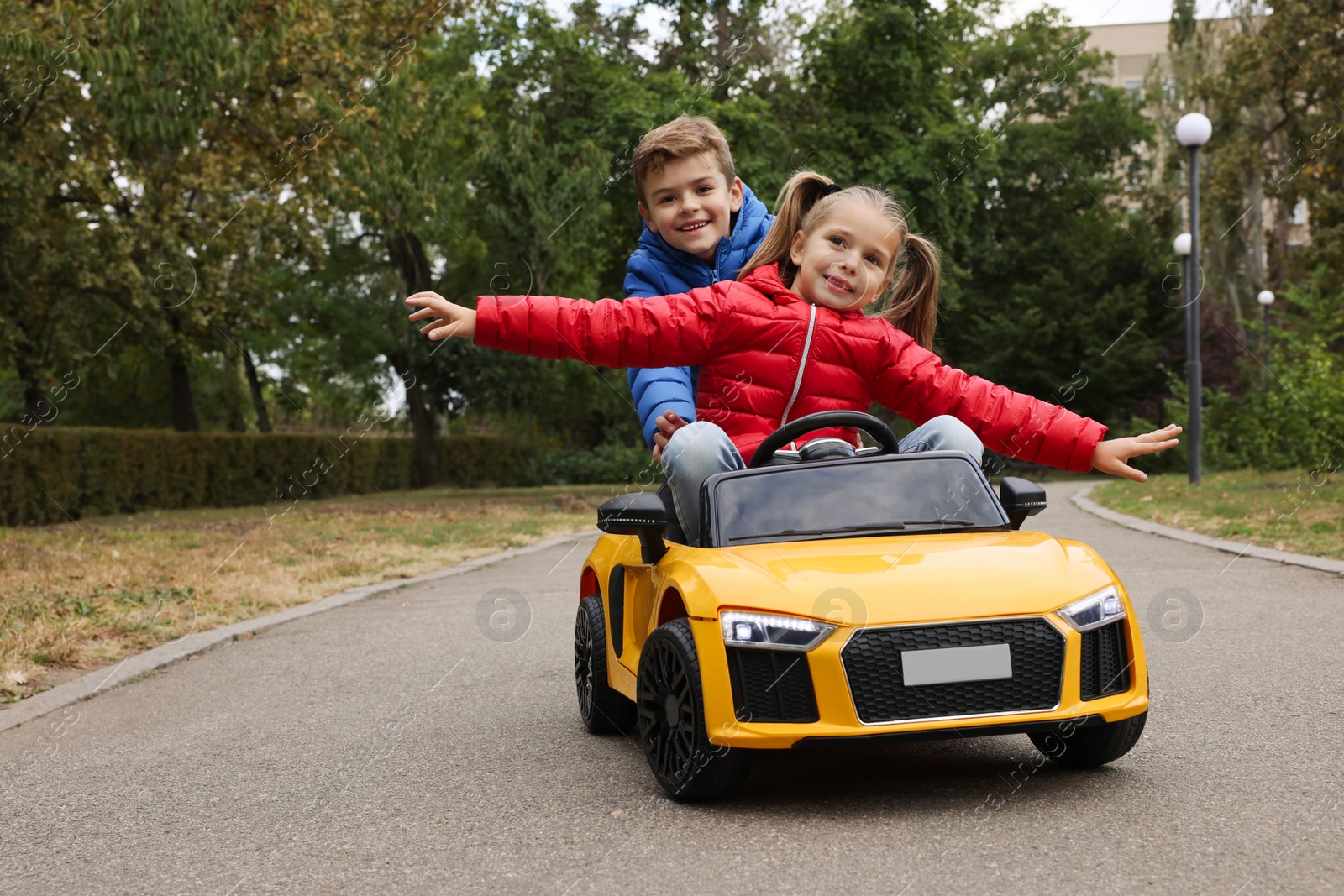 Photo of Cute boy pushing children's car with little girl outdoors. Space for text