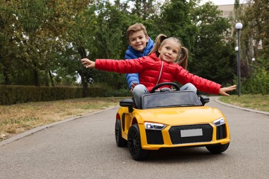 Photo of Cute boy pushing children's car with little girl outdoors. Space for text