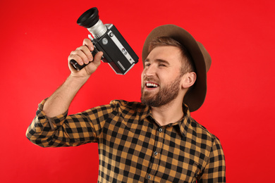 Young man with vintage video camera on red background