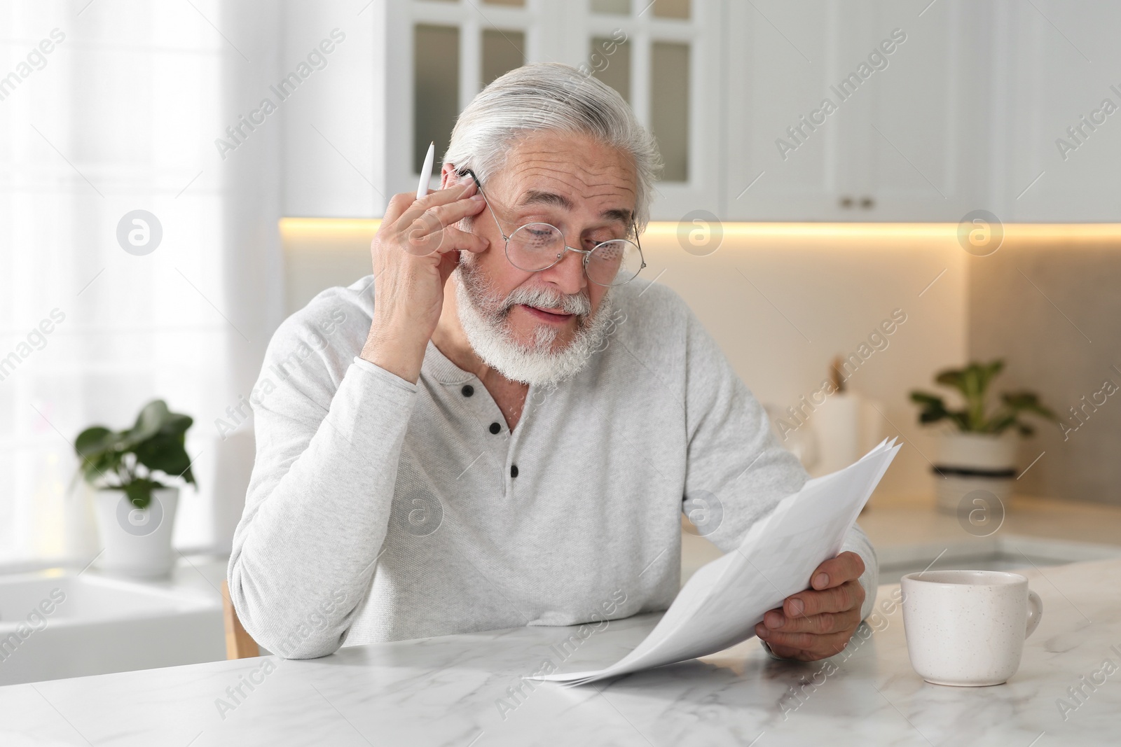 Photo of Senior man solving crossword at table in kitchen
