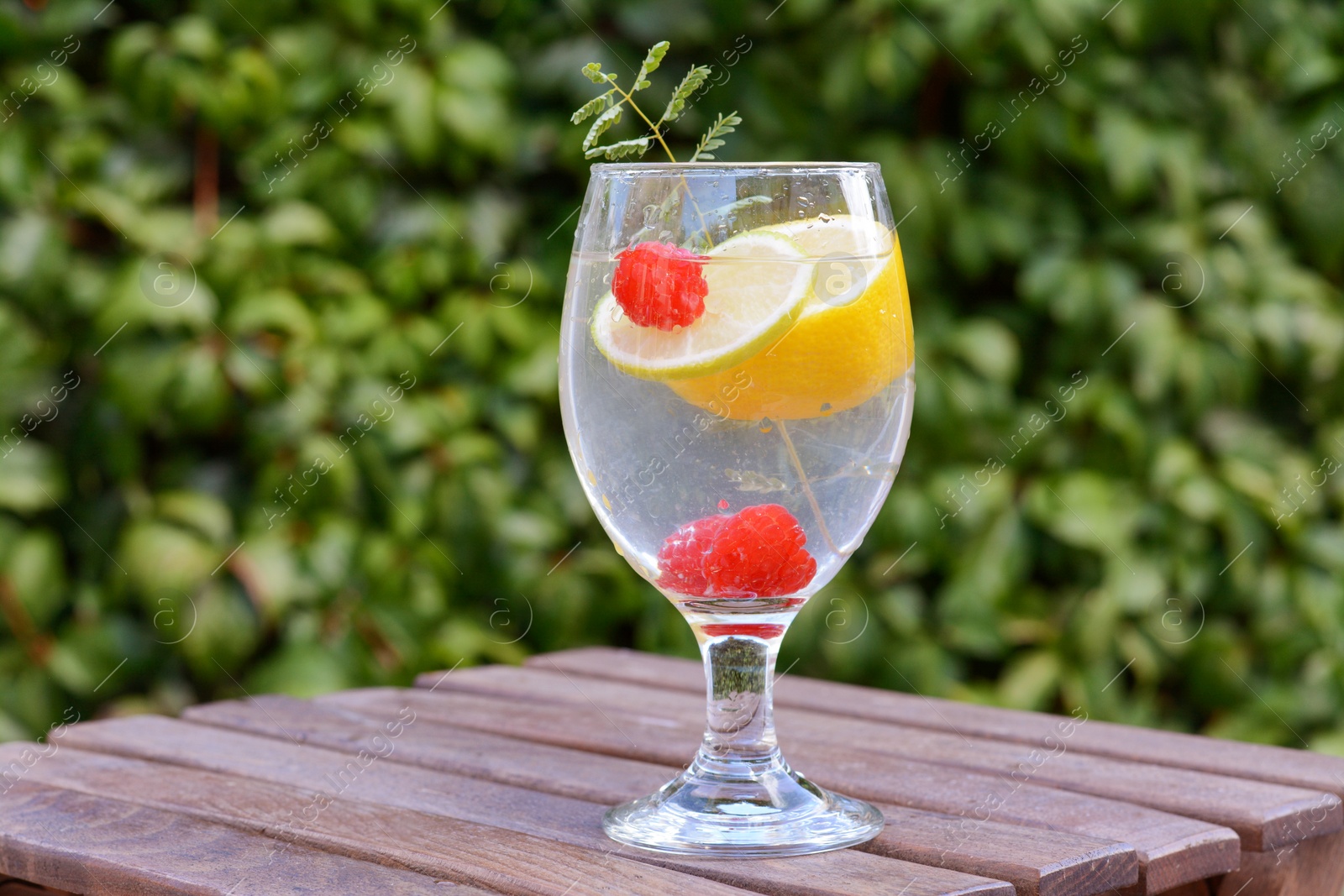 Photo of Delicious refreshing lemonade with raspberries on wooden table outdoors