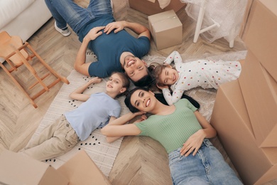 Photo of Happy family lying on floor near moving boxes in new house, top view
