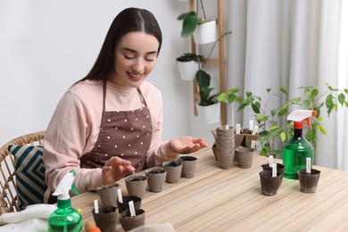 Woman planting vegetable seeds into peat pots with soil at wooden table indoors