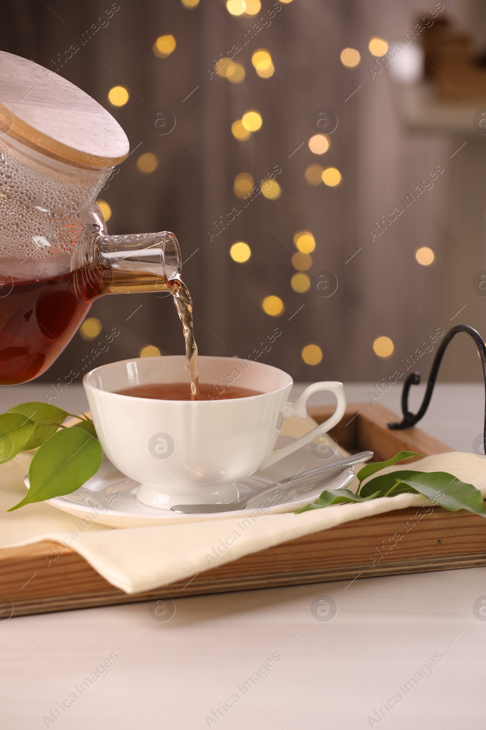 Photo of Pouring aromatic tea into cup at light wooden table, closeup