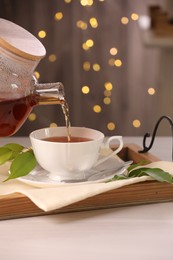 Photo of Pouring aromatic tea into cup at light wooden table, closeup