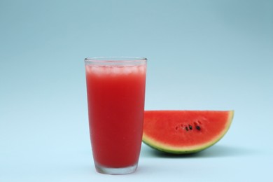 Photo of Glass of delicious drink with ice cubes and cut fresh watermelon on light blue background
