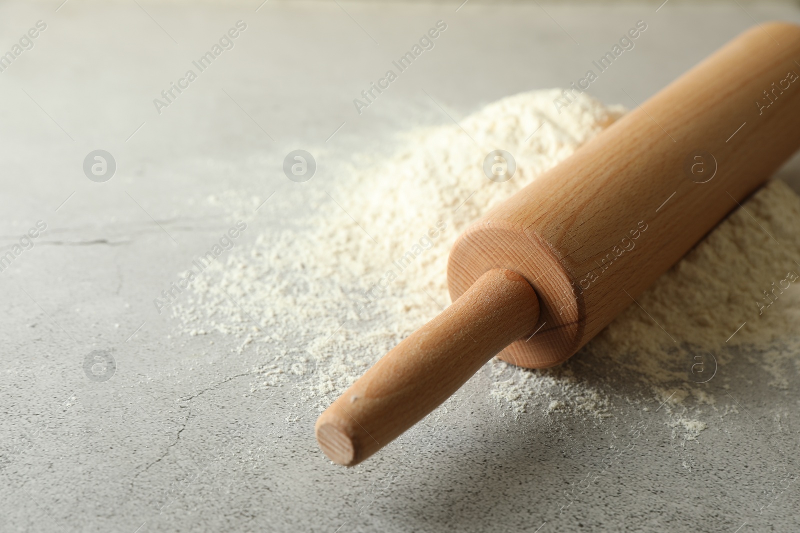 Photo of Flour and rolling pin on grey table, closeup. Space for text