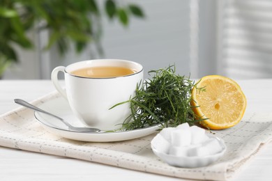 Photo of Aromatic herbal tea, fresh tarragon sprigs, sugar cubes and lemon on white wooden table