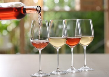 Photo of Pouring rose wine from bottle into glass on table against blurred background