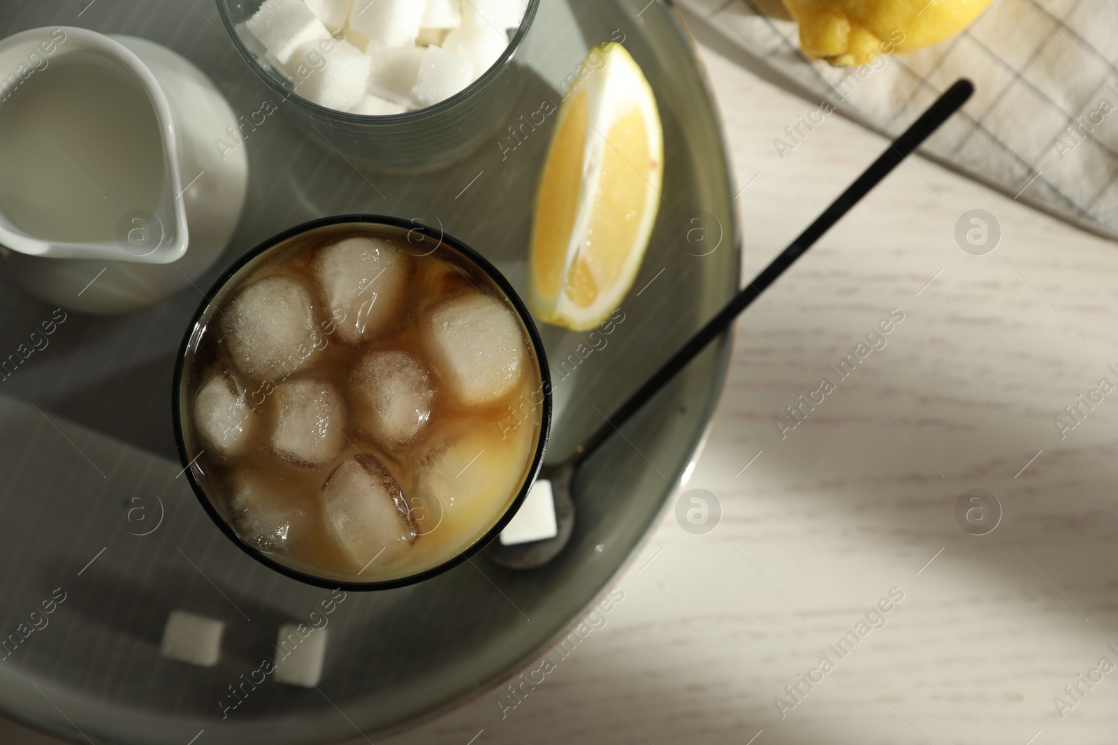 Photo of Refreshing iced coffee with milk in glass, sugar cubes and spoon on white wooden table, top view. Space for text