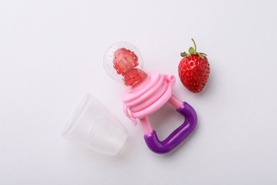 Photo of Nibbler with fresh strawberries on white background, flat lay. Baby feeder
