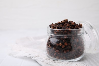 Photo of Aromatic cloves in glass jar on white table, closeup. Space for text