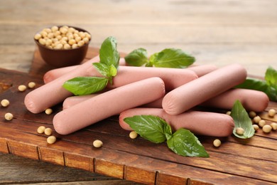 Photo of Fresh raw vegetarian sausages with basil and soybeans on wooden board, closeup