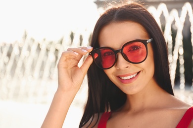 Photo of Beautiful young woman wearing stylish sunglasses outdoors