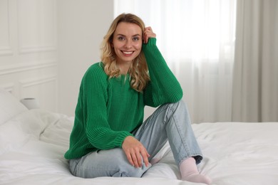 Photo of Happy woman in stylish warm sweater on bed at home