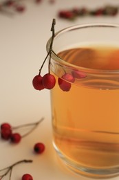 Photo of Cup with hawthorn tea and berries on beige table, closeup