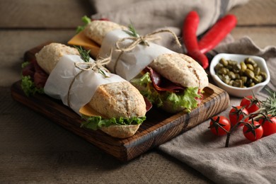 Photo of Delicious sandwiches with bresaola, lettuce and other products on wooden table