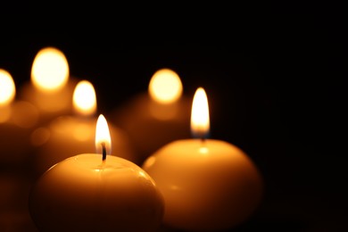 Photo of Many burning wax candles on black background, closeup