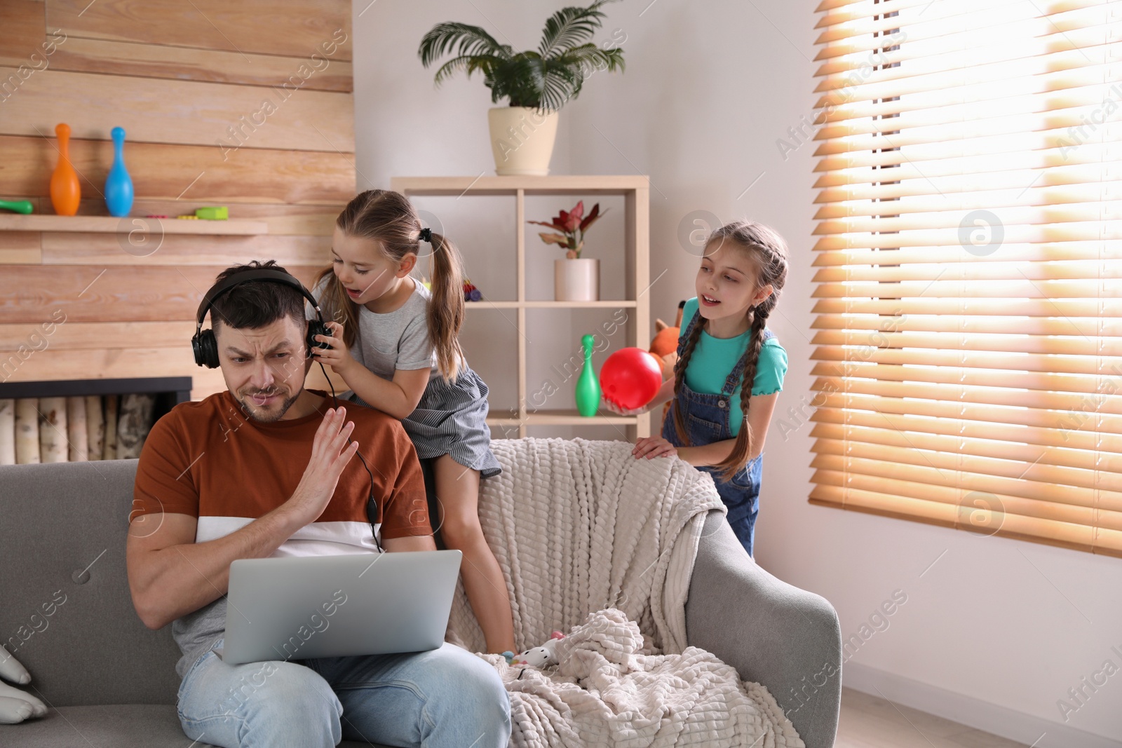 Photo of Children disturbing stressed man in living room. Working from home during quarantine