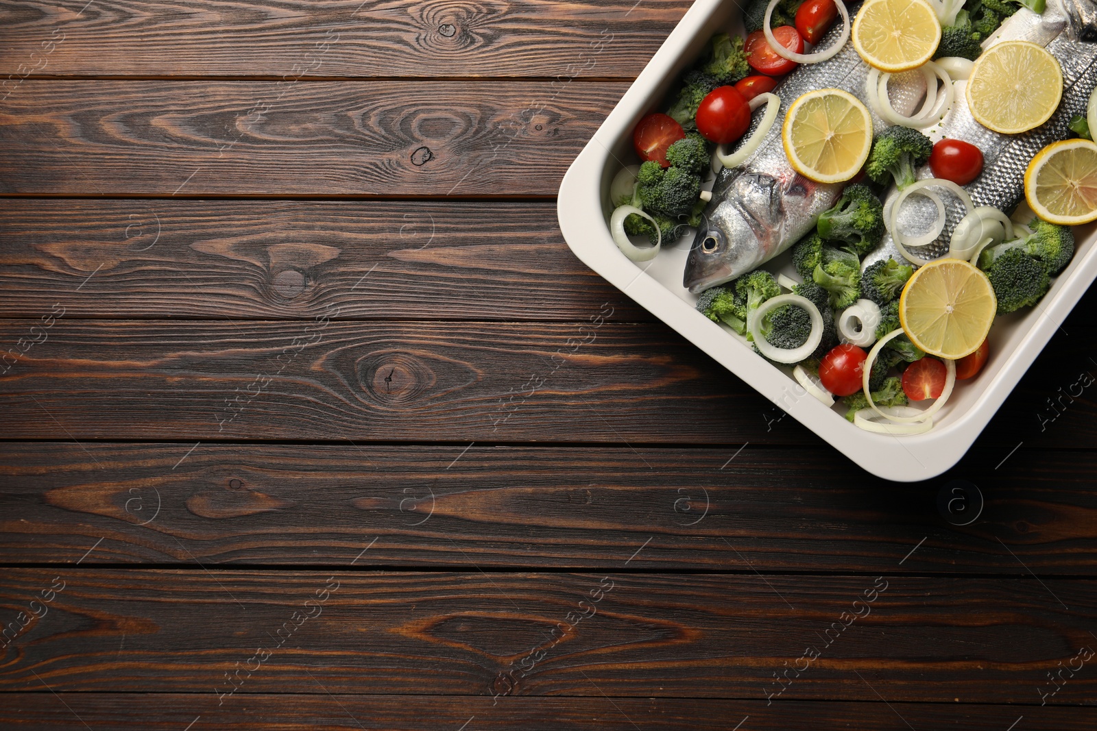 Photo of Raw fish with vegetables and lemon in baking dish on wooden table, top view. Space for text