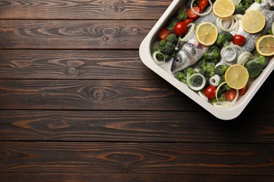 Photo of Raw fish with vegetables and lemon in baking dish on wooden table, top view. Space for text