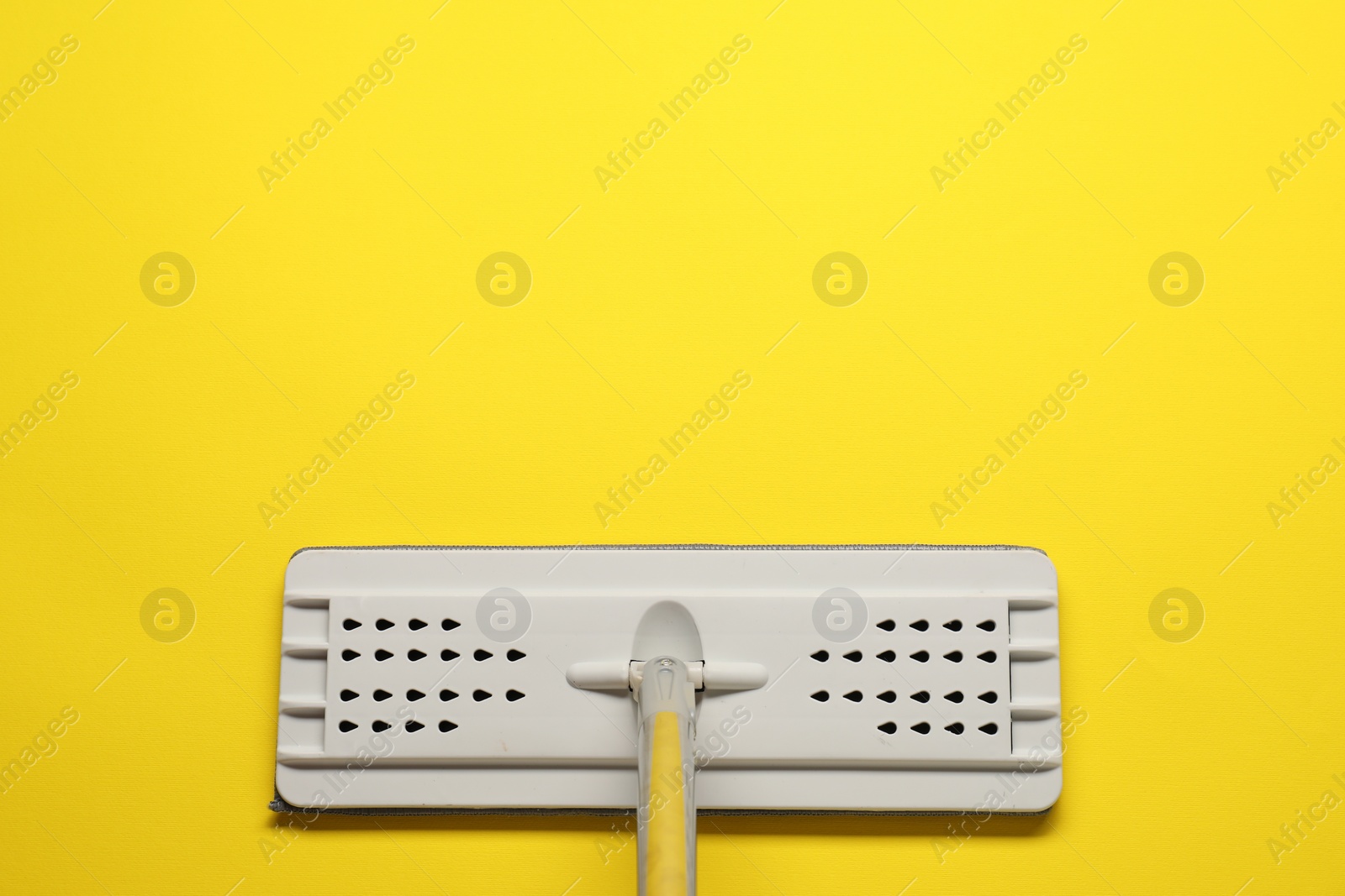 Photo of Mop with metal handle on yellow background, top view. Space for text