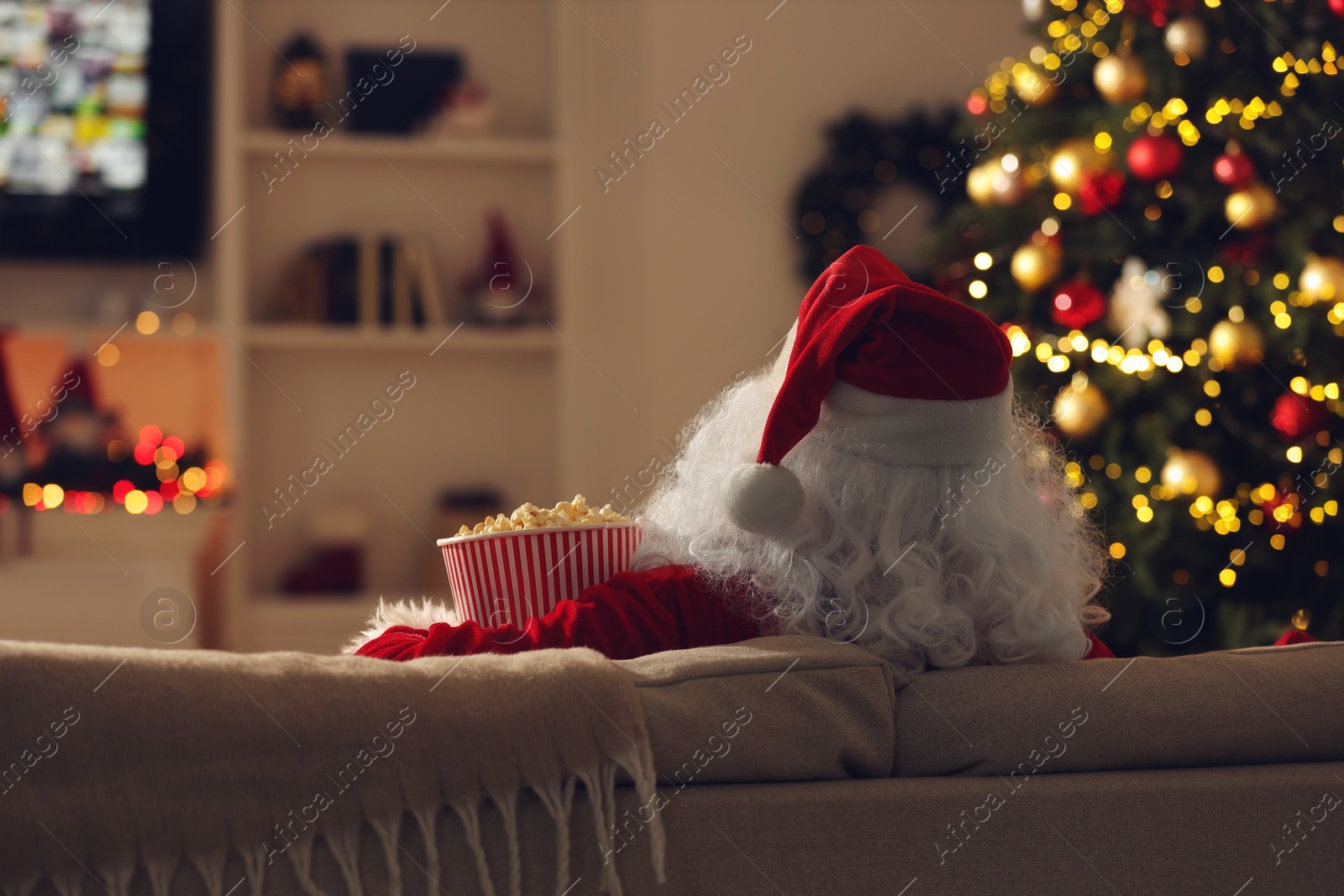 Photo of Merry Christmas. Santa Claus with popcorn bucket watching TV on sofa at home, back view