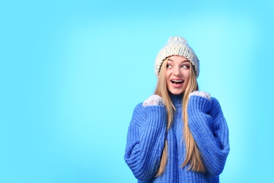 Portrait of emotional young woman in stylish hat, sweater and mittens on color background, space for text. Winter atmosphere