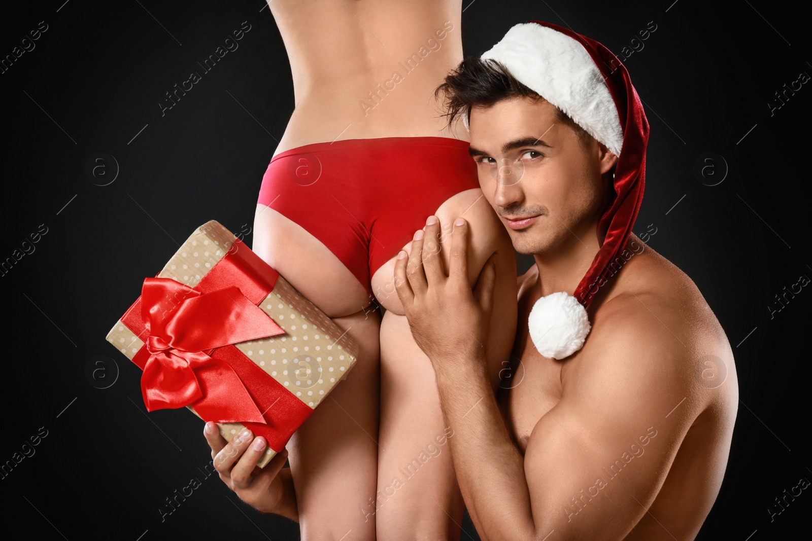 Photo of Attractive young Santa Claus with sexy woman and gift on dark background