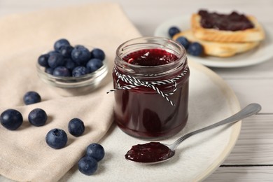 Photo of Delicious blueberry jam and fresh berries on white wooden table