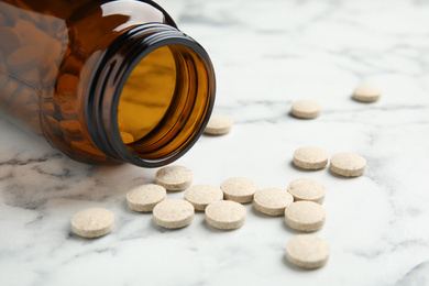 Bottle with vitamin pills on white marble table, closeup