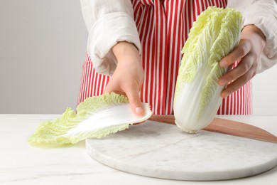 Photo of Woman separating leaf from fresh chinese cabbage at white marble table, closeup