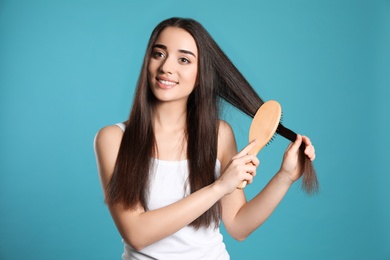 Beautiful smiling young woman with hair brush on color background