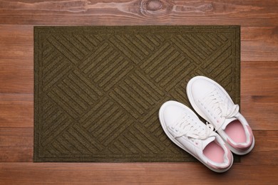 Photo of New clean door mat with shoes on wooden floor, flat lay