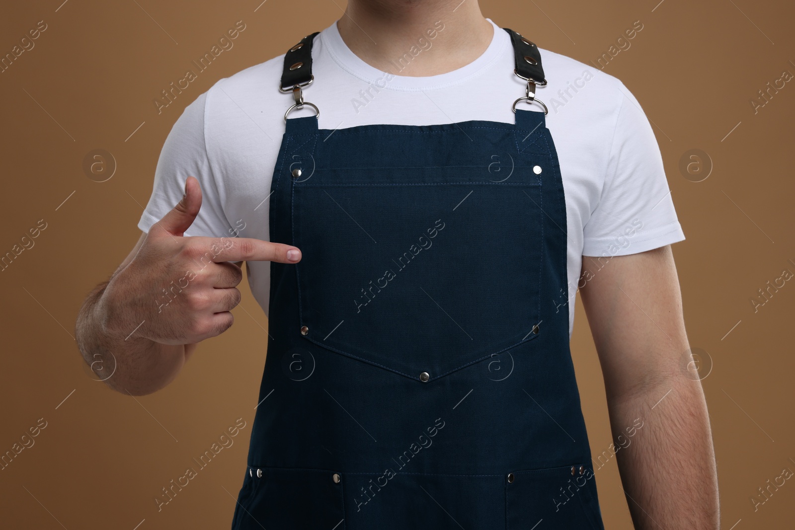 Photo of Man pointing at kitchen apron on brown background, closeup. Mockup for design