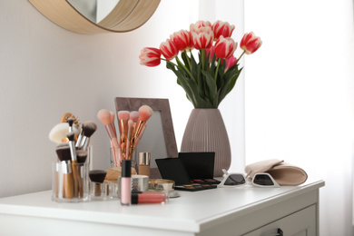 Photo of Dressing table with makeup products, accessories and tulips indoors. Interior element