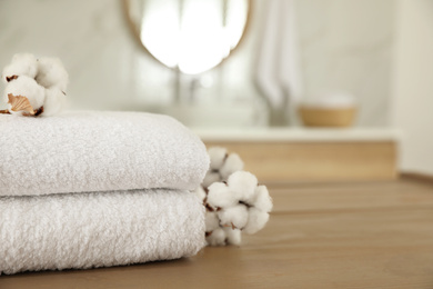 Photo of Stack of clean towels and cotton flowers on wooden table in bathroom. Space for text