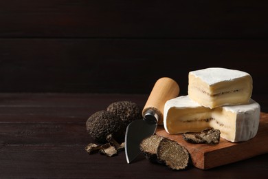 Photo of Delicious cheese, fresh black truffles and knife on wooden table. Space for text