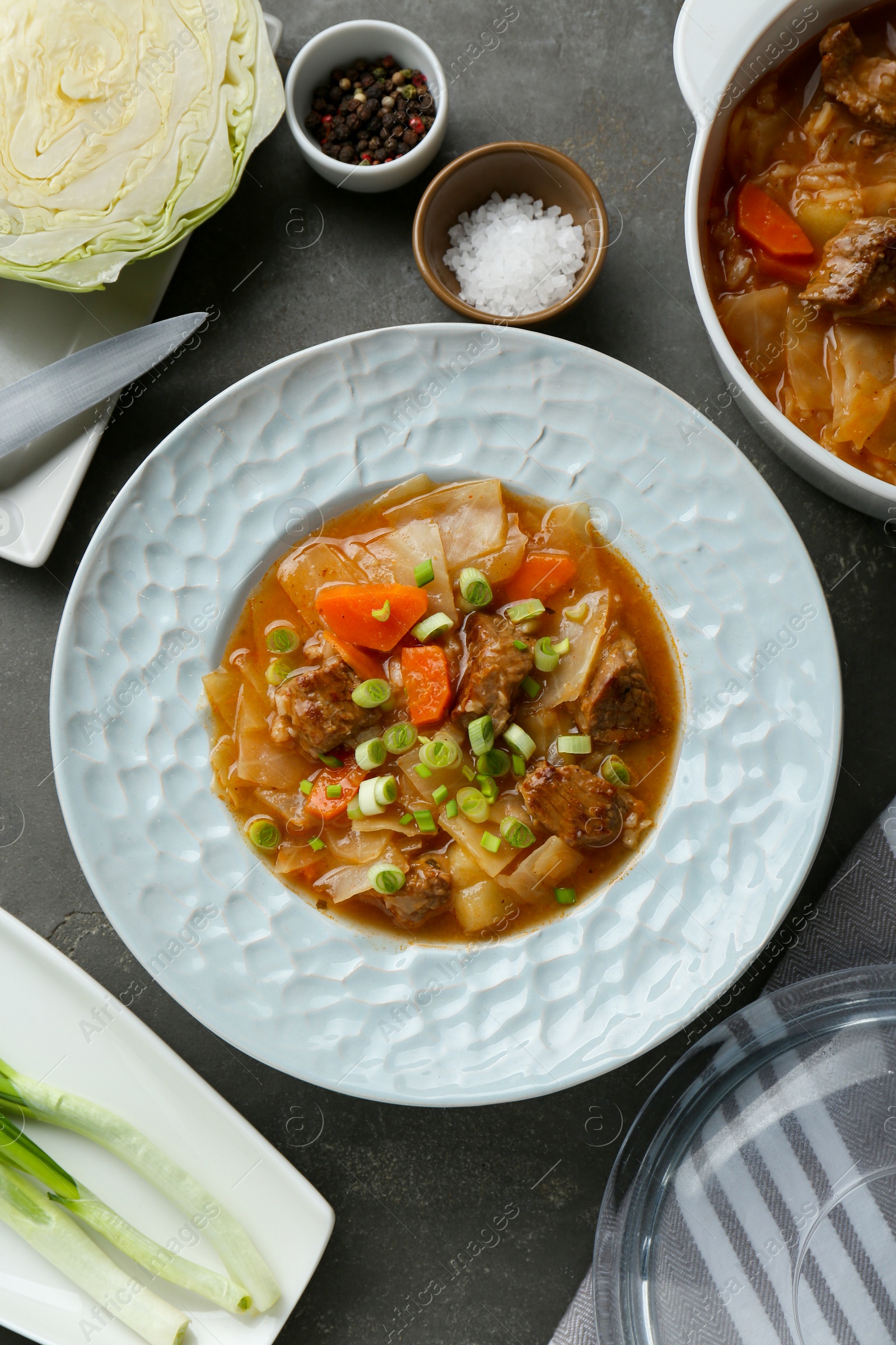 Photo of Tasty cabbage soup and ingredients on grey table, flat lay