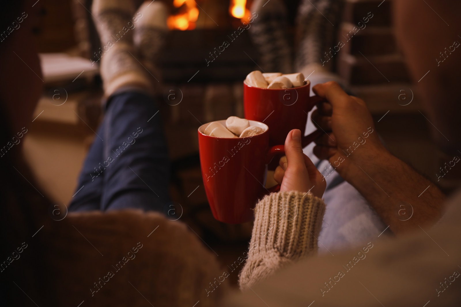 Photo of Lovely couple with sweet cocoa near fireplace indoors, closeup