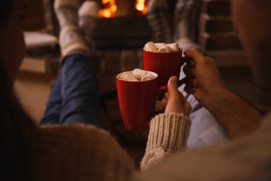 Photo of Lovely couple with sweet cocoa near fireplace indoors, closeup