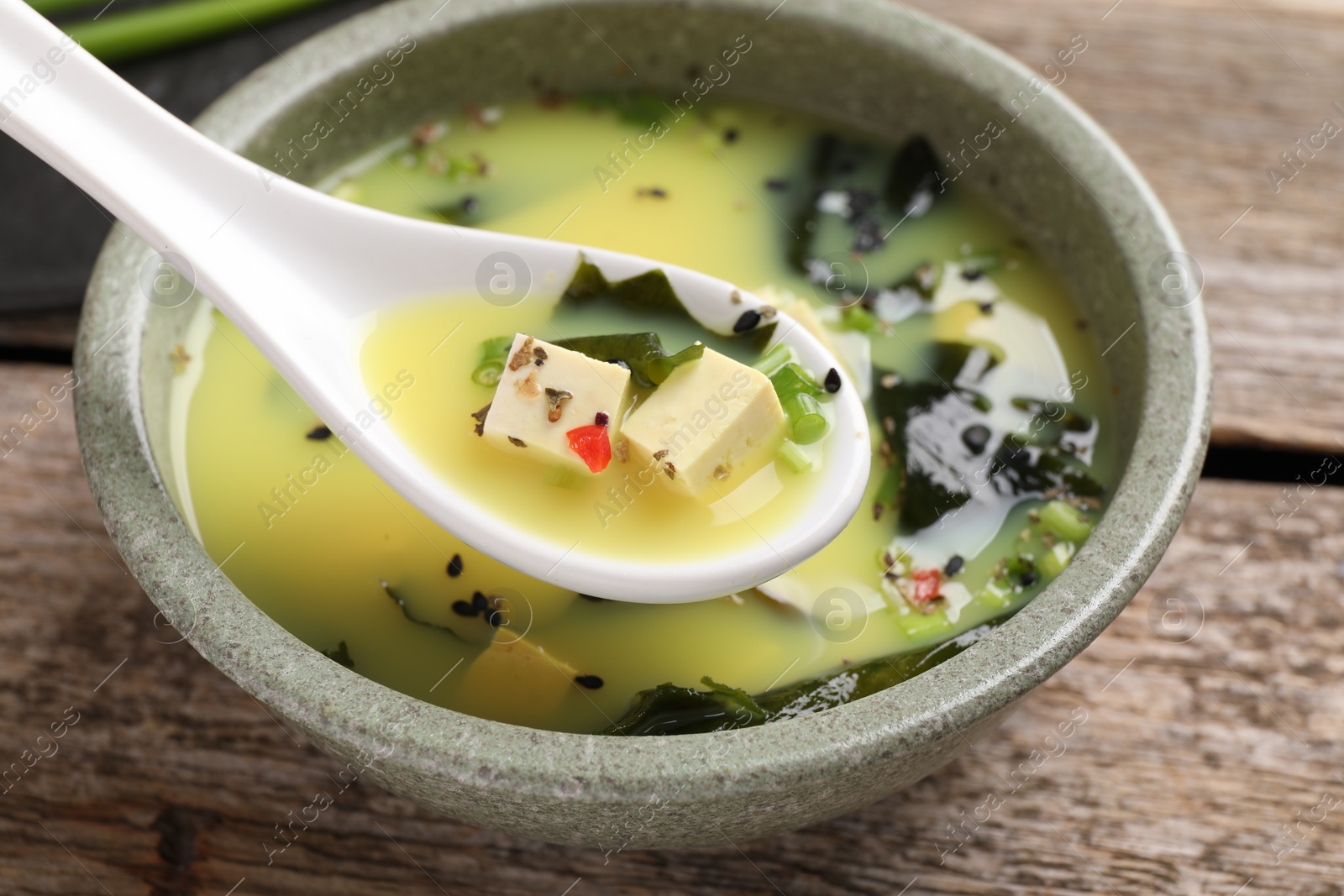 Photo of Delicious miso soup with tofu in spoon above bowl, closeup