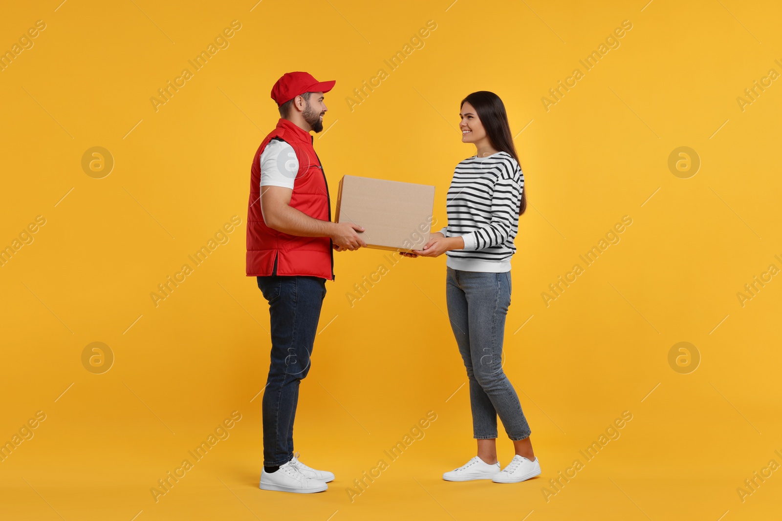 Photo of Smiling courier giving parcel to receiver on orange background