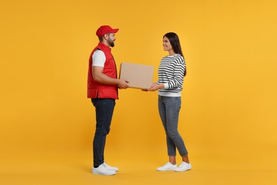 Photo of Smiling courier giving parcel to receiver on orange background