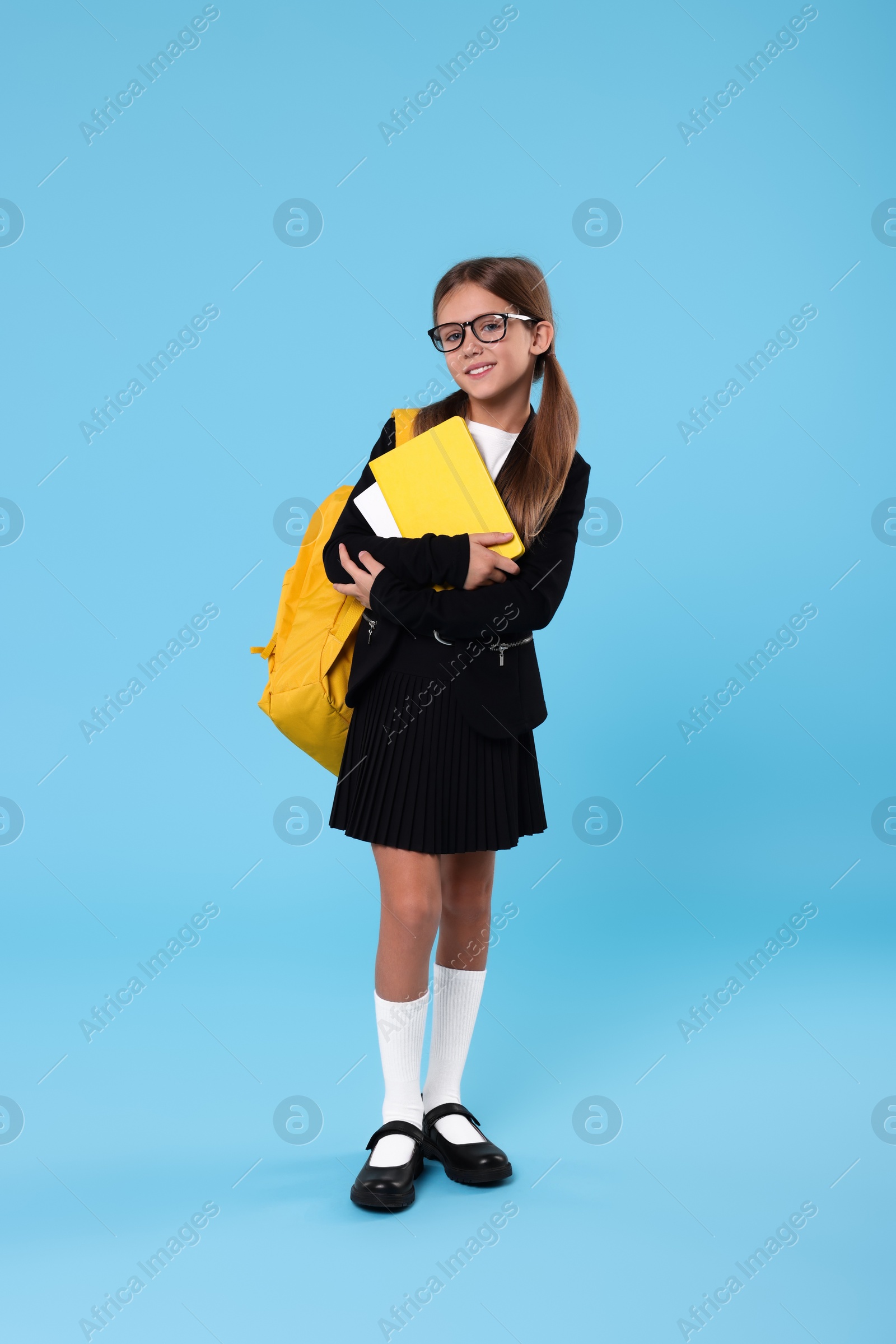 Photo of Happy schoolgirl with backpack and books on light blue background