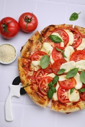 Photo of Delicious Caprese pizza with tomatoes, mozzarella and basil on white tiled table, flat lay