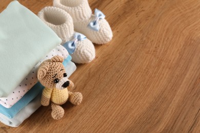 Photo of Stack of baby boy's clothes, booties and toy on wooden table, above view. Space for text
