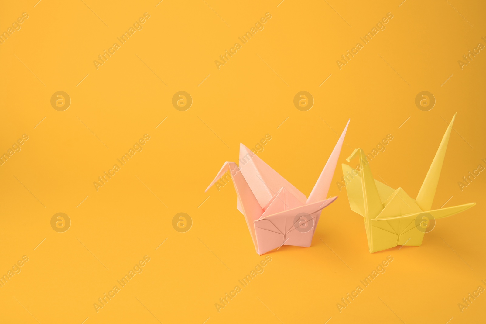 Photo of Origami art. Beautiful pale pink and light yellow paper cranes on orange background, space for text