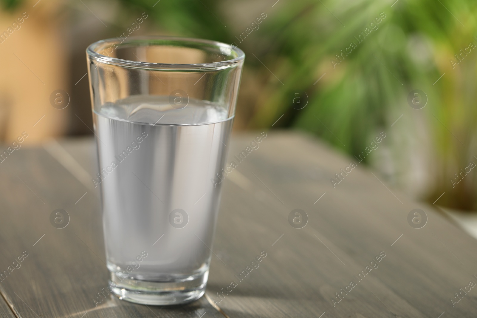 Photo of Glass of pure water on wooden table against blurred background, space for text