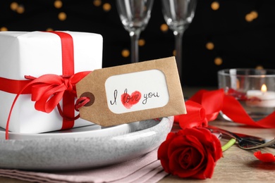 Photo of Beautiful place setting and tag with phrase I Love You on table against blurred lights, closeup. Valentine's day romantic dinner